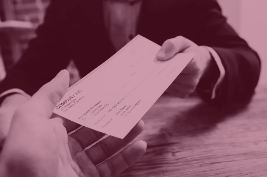 Red-tinted photo of a hand passing a paycheck across a desk.