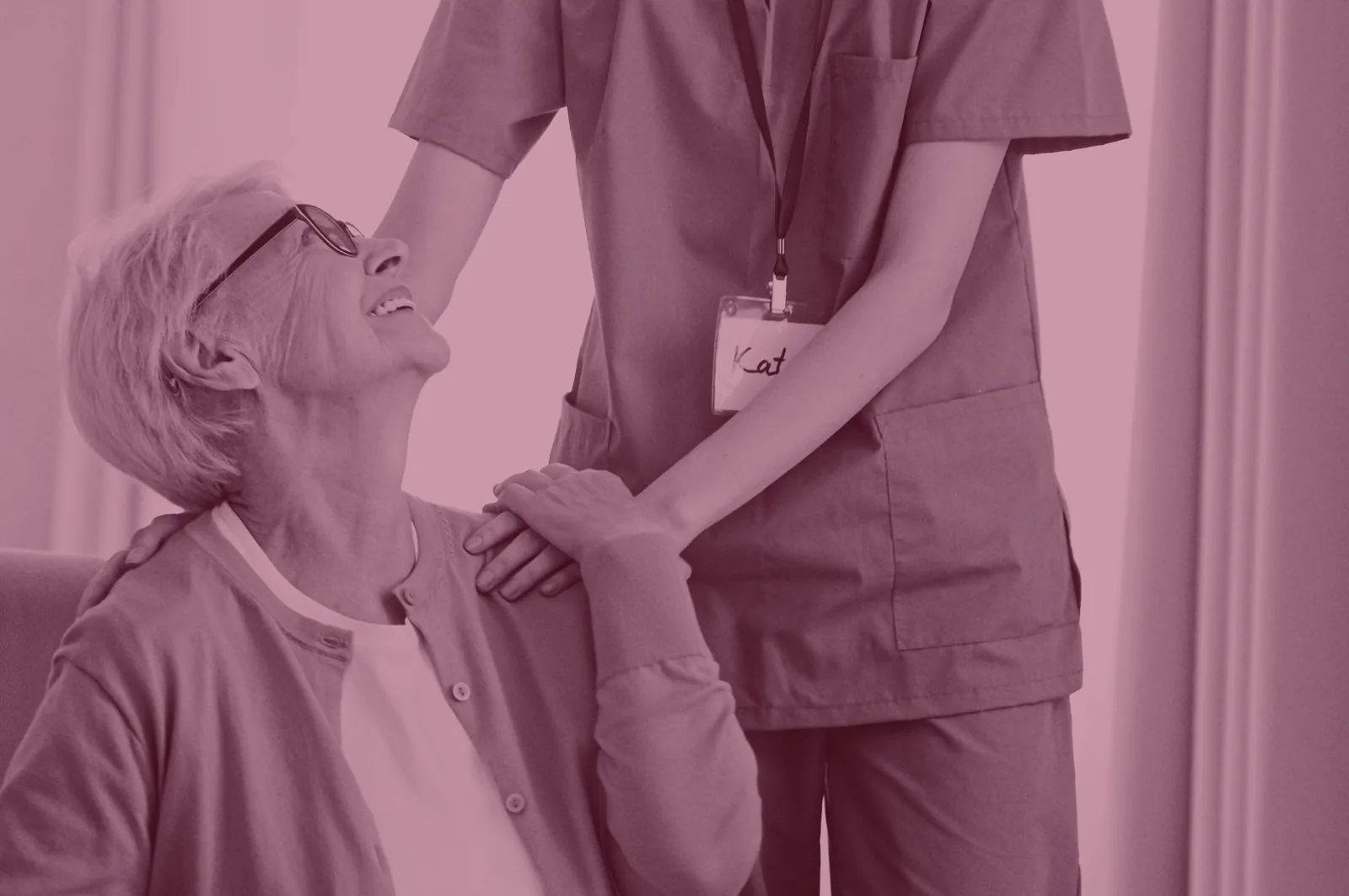 Red-tinted photo of a caregiver in scrubs holding the hand of a smiling older woman.