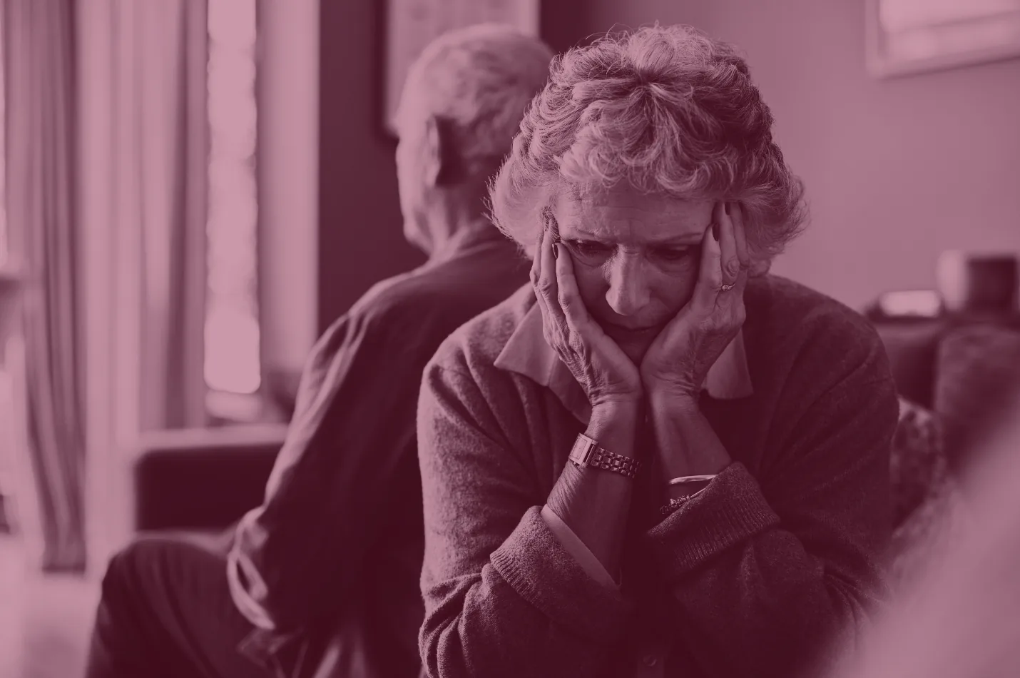 Red-tinted photo of a worried older woman resting her head in her hands.